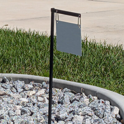 Low arm sign post installed in a landscaped area near a sidewalk for small outdoor signage.